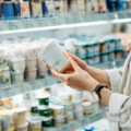 Cropped shot of young woman shopping in the dairy section of a supermarket. She is reading the nutrition label on a container of fresh organic healthy natural yoghurt