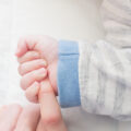 holding the finger of a father or mother tightly with the baby's hand on white blanket