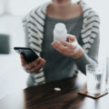 Close up of young Asian woman holding a pill bottle, consulting to her family doctor online in a virtual appointment over the smartphone at home