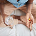 High angle close up of unrecognizable African-American woman holding pills or vitamins in open hand while taking morning medication, copy space