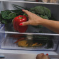 Close up shot of unrecognizable woman putting a red bell pepper on the shelf in her fridge while unloading groceries.
