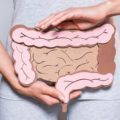 partial view of person holding paper made large intestine on grey background