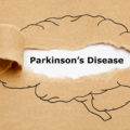 Concept with text Parkinsons Disease appearing behind torn brown paper with human brain drawing.