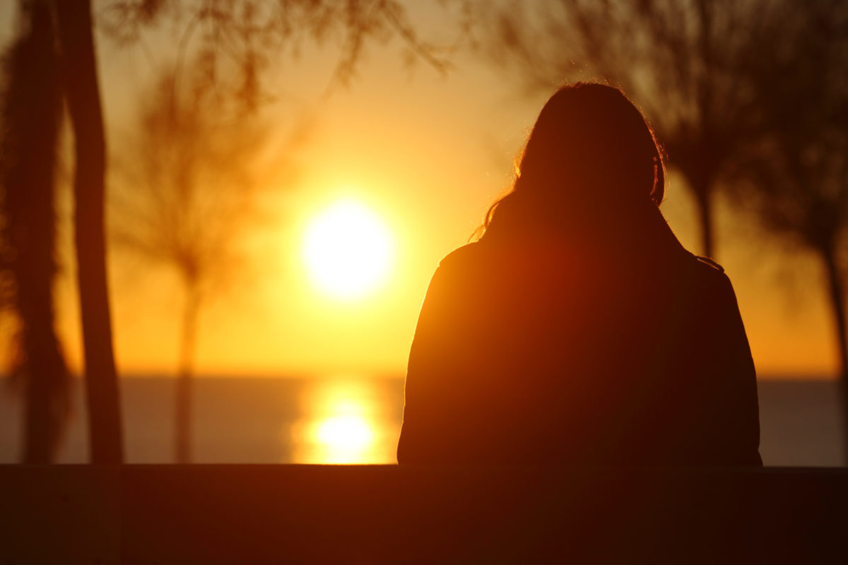Back view portrait of a silhouette of a lonely woman watching sunset in winter