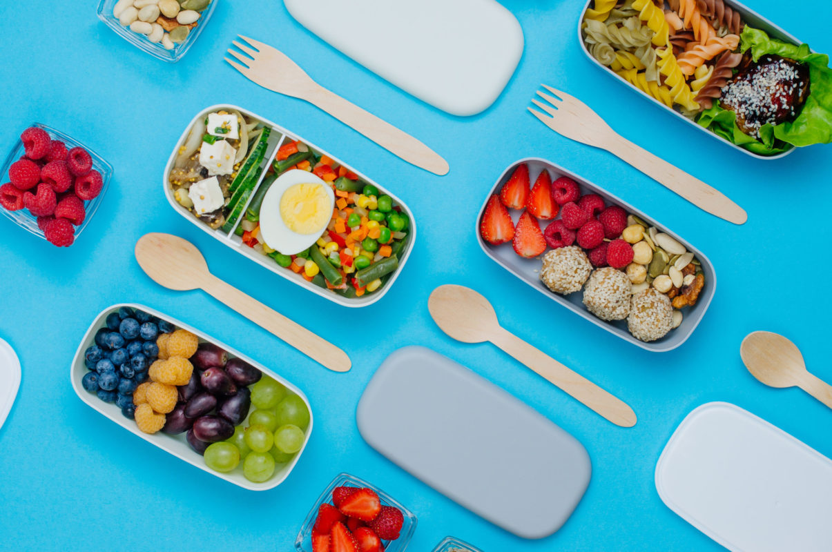 Pattern of plastic lunch boxes filled with healthy food, fresh fruits and berries on blue background. Top view, flat lay.