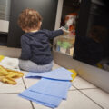 Baby boy opens up kitchen cupboard and pulls out various cleaning products from under the sink while his parents are distracted.