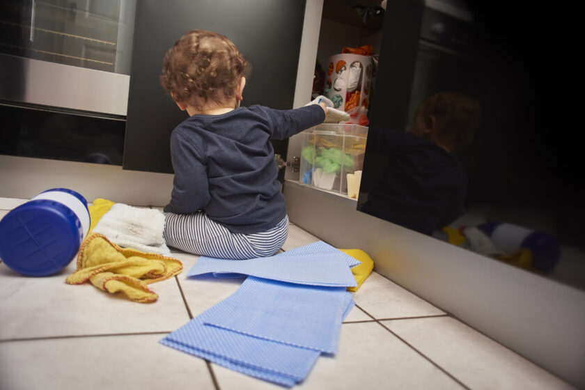 Baby boy opens up kitchen cupboard and pulls out various cleaning products from under the sink while his parents are distracted.