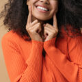 Close up portrait of young happy African American woman pointing finger on white teeth isolated on background. Health care, dental treatment concept