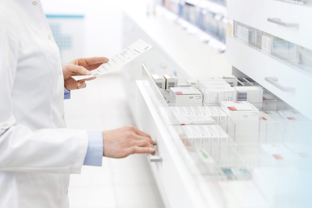 pharmacist holding a prescription while pulling open a drawer of medications