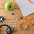 healthy plan with notebook and pencil on wooden table with apple, tape measure and stethoscope. Top view.