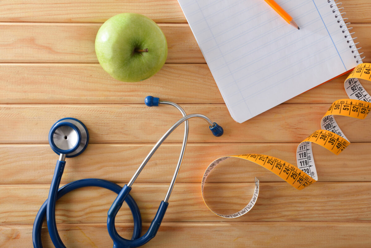 healthy plan with notebook and pencil on wooden table with apple, tape measure and stethoscope. Top view.