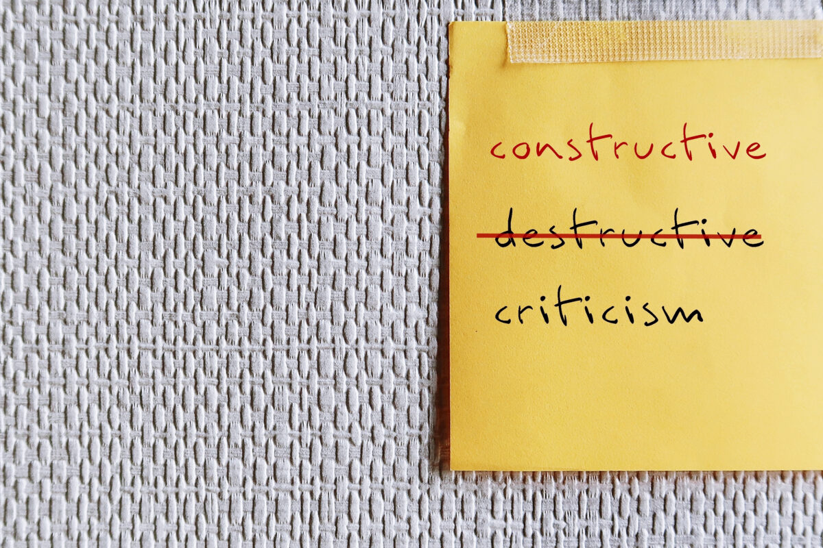 Note stick on copy space office wallpaper with handwritten DESTRUCTIVE CRITICISM, changed to CONSTRUCTIVE CRITICISM - means to shift focus on negative to be on building up other person