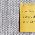 Note stick on copy space office wallpaper with handwritten DESTRUCTIVE CRITICISM, changed to CONSTRUCTIVE CRITICISM - means to shift focus on negative to be on building up other person