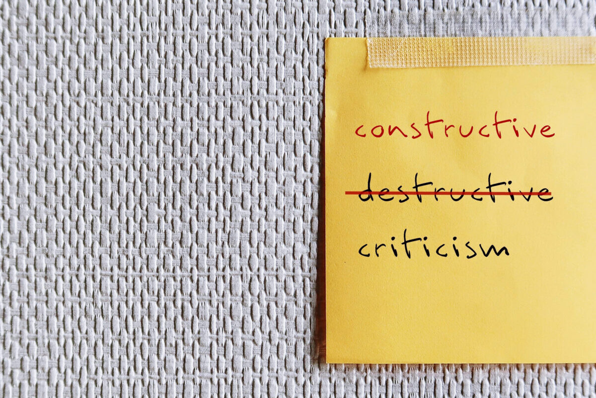 Note stick on copy space office wallpaper with handwritten DESTRUCTIVE CRITICISM, changed to CONSTRUCTIVE CRITICISM - means to shift focus on negative to be on building up other person