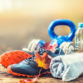 Pair of blue sport shoes water and dumbbells laid on a wooden board in a tree autumn alley with maple leaves - accessories for run exercise or workout activity.