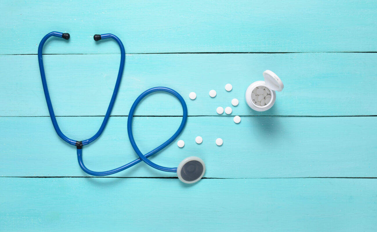 Stethoscope and bottle with pills on a blue wooden background, medical concept, top view