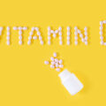 Vitamin D pills dropped from bottle on yellow background. Flat lay, top view, free copy space.