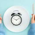person holding fork and knife next to a plate with a clock on it