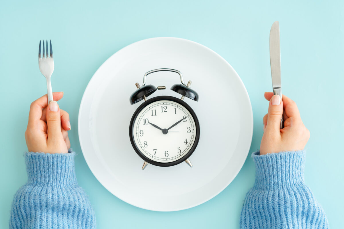 person holding fork and knife next to a plate with a clock on it