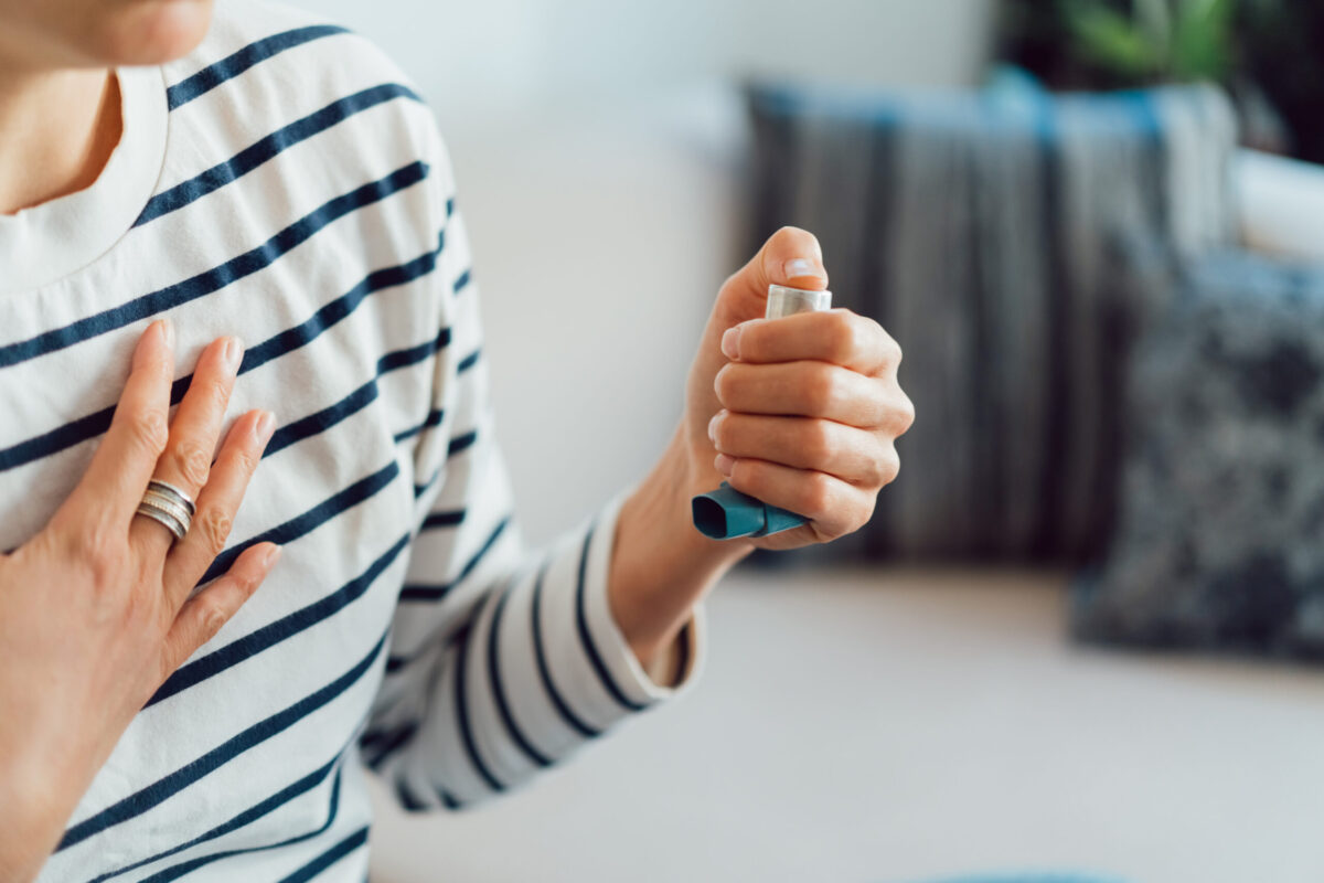 Woman using an asthma inhaler indoors. Using medication during an asthma attack.
