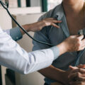 Doctor is using a stethoscope listen to the heartbeat of a male patient.