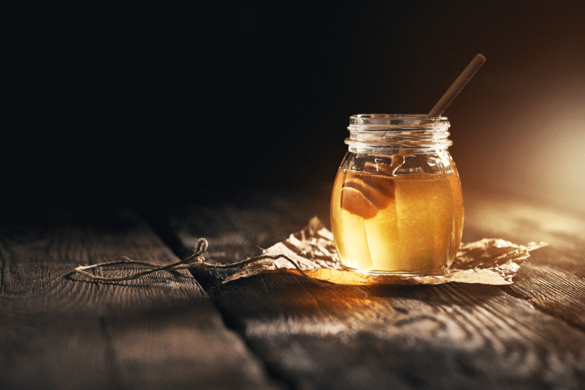Jar of camomile honey on black background with bamboo dipper on wooden table.