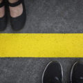 Legs of a couple standing opposite each other divided by the yellow asphalt line top view