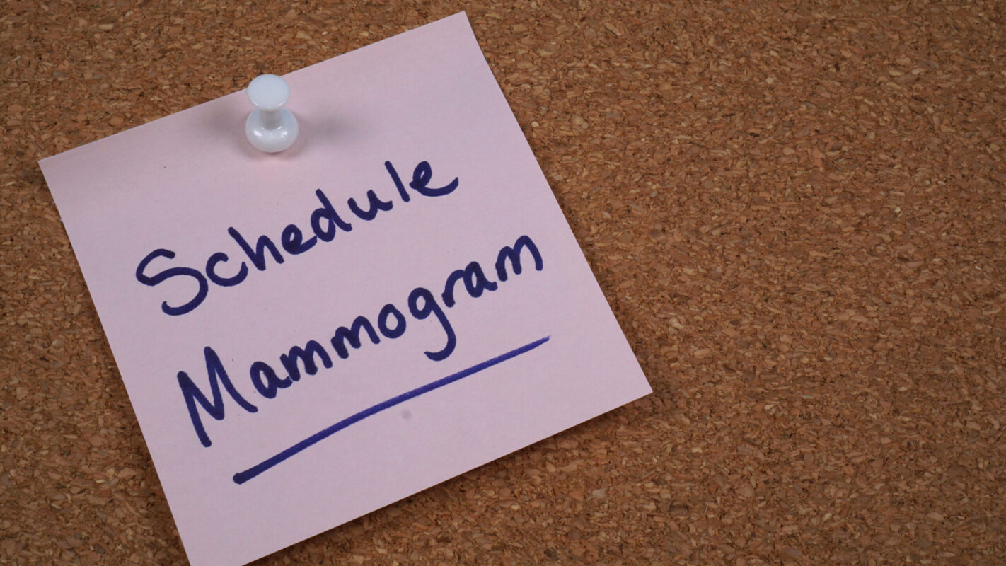 Sticky note reminder to schedule mammogram posted to cork message board.