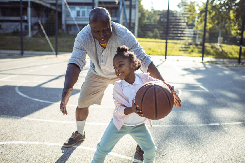 Grandfather and granddaughter playing basketball together on an outdoors basketball court