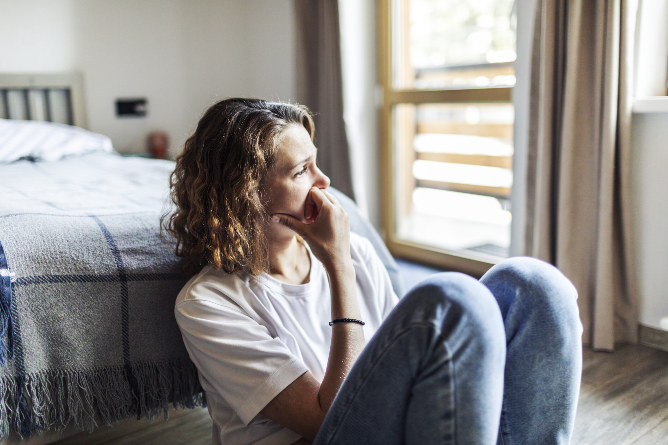 Female sitting at the foot of a bed with worrisome look.