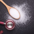 White salt in wooden spoon and doctor stethoscope on black stone table background.