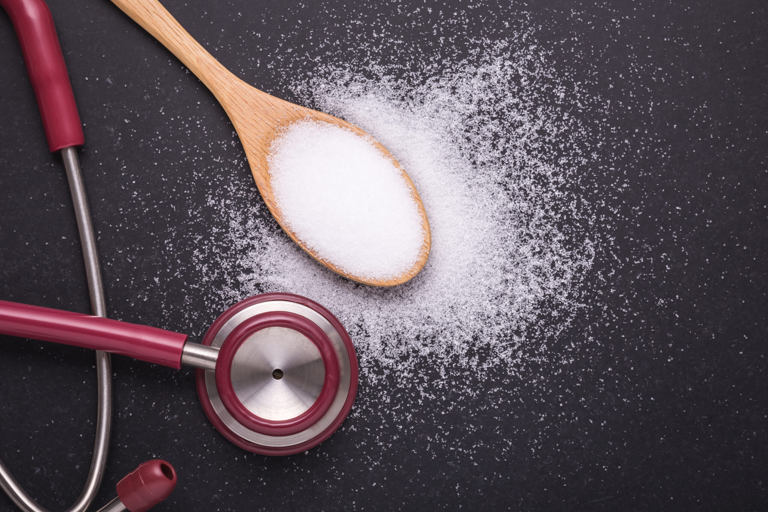 White salt in wooden spoon and doctor stethoscope on black stone table background.