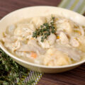 A bowl of chicken and dumplings with a sprig of thyme on top.