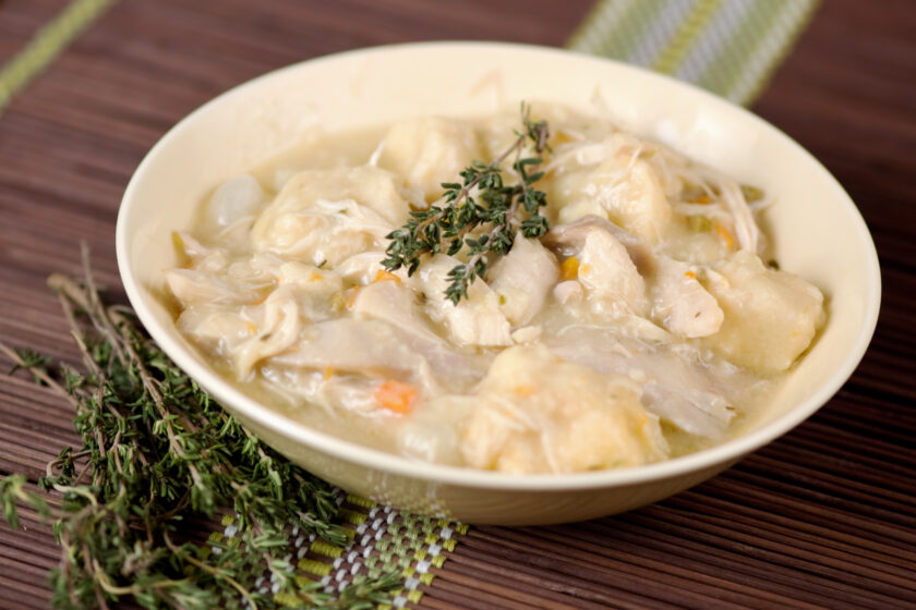 A bowl of chicken and dumplings with a sprig of thyme on top.