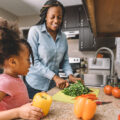 Daughter looking at mother cut vegetables.