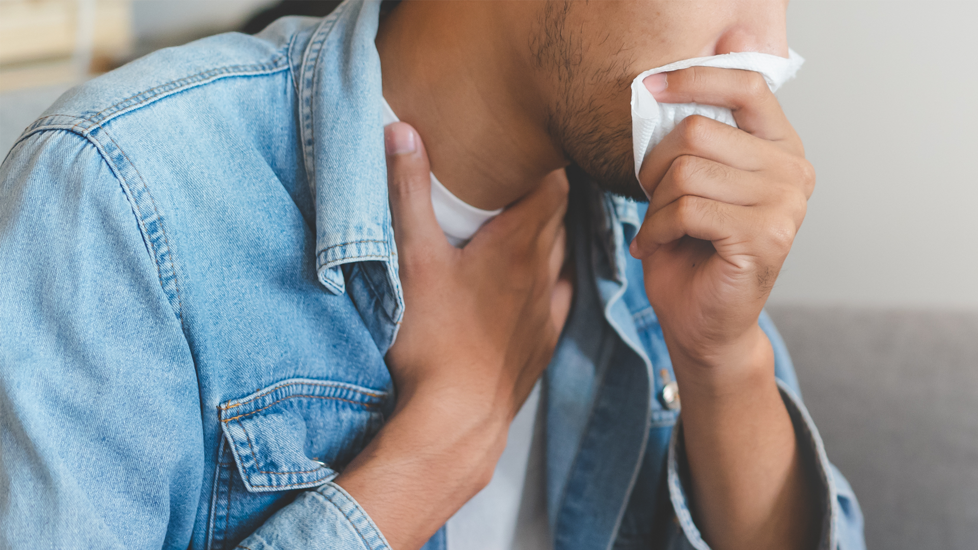 person coughing into a tissue and holding throat.