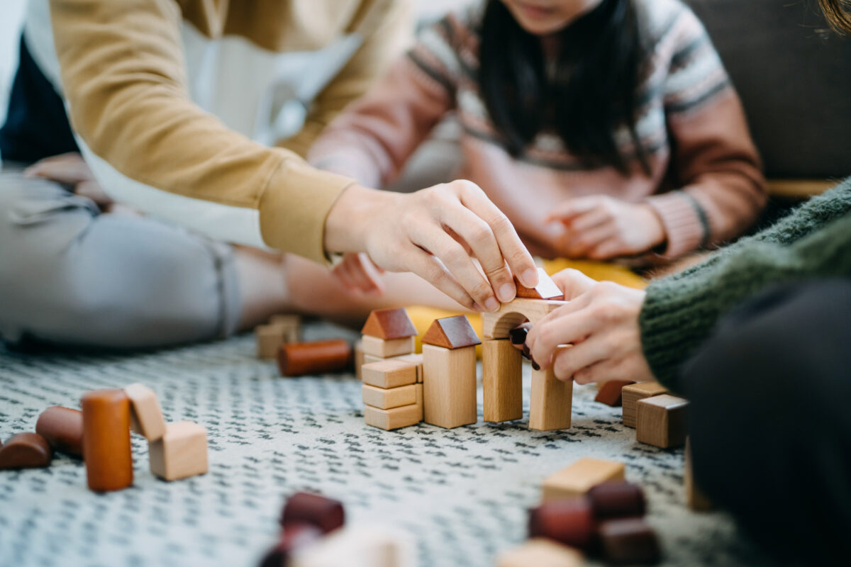 Photo of Close up of parents sitting on the floor in the living room playing with wooden building blocks.