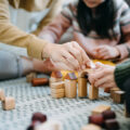 Photo of Close up of parents sitting on the floor in the living room playing with wooden building blocks.