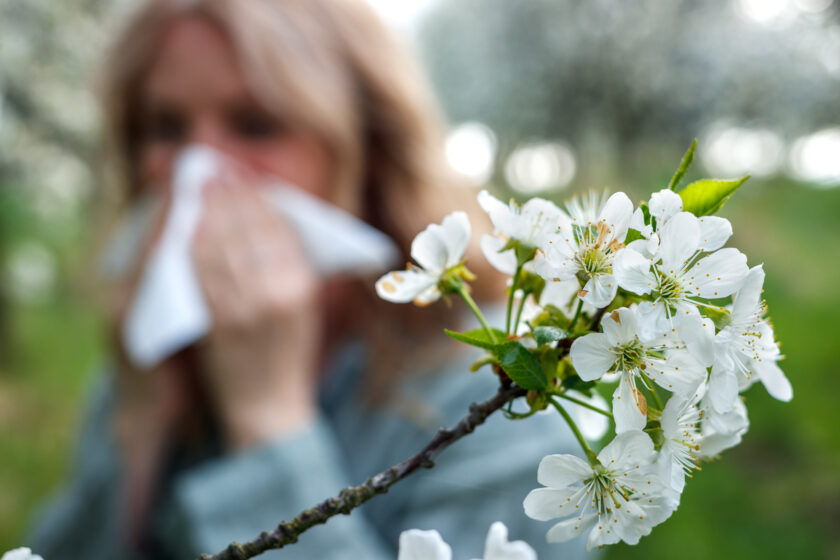 Woman sneezing and blowing nose outdoors at springtime.