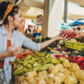 A young woman buys vegetables and fruits at the market .