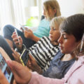 Four children sat on sofa looking at phones and tablets