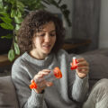 Young adult woman takes her asthma medication with an inhaler while sitting on a sofa in living room