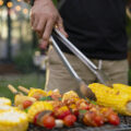 Person grilling corn on the cob and kebabs.