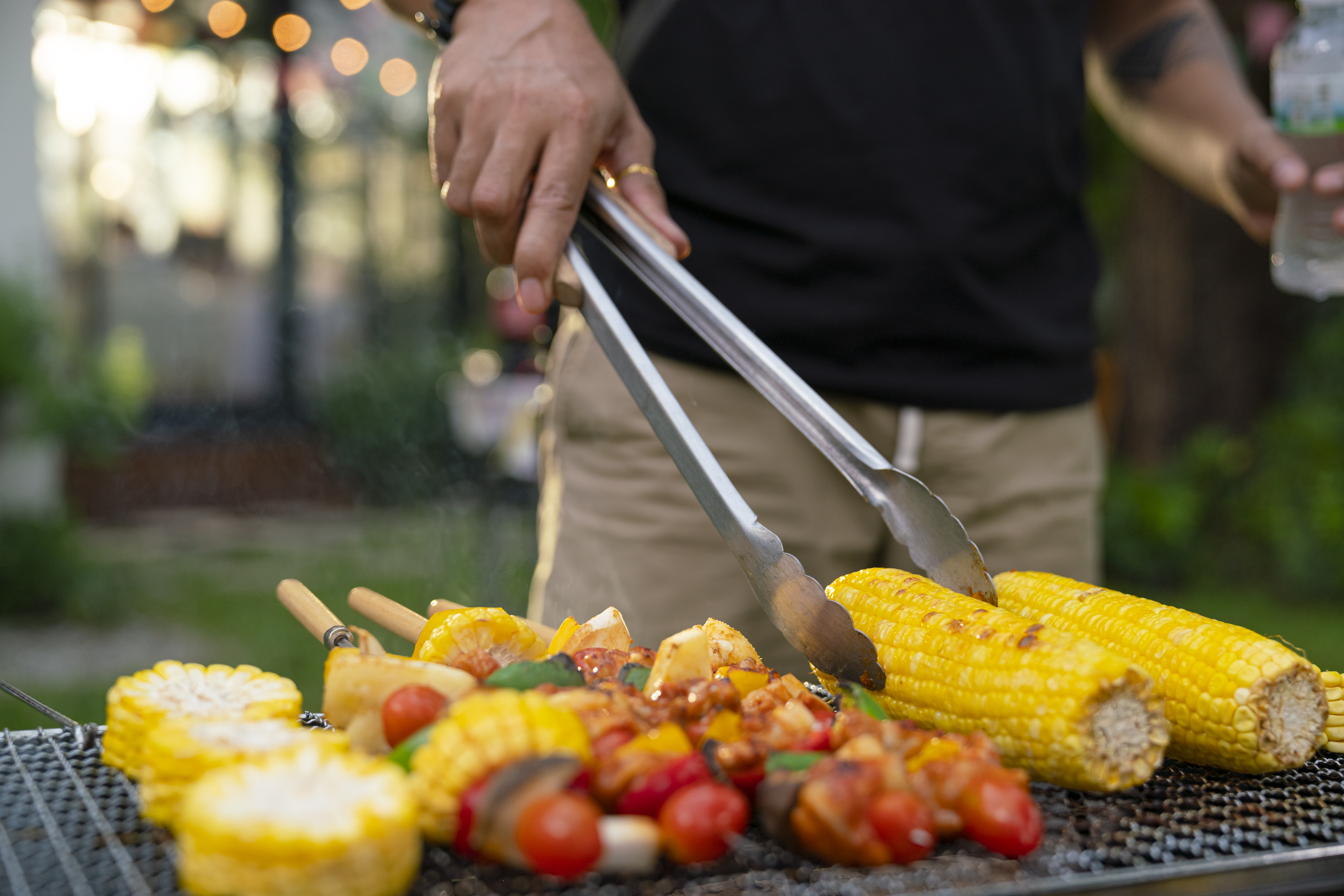 Person grilling corn on the cob and kebabs.