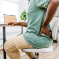 Tired young black man working from home on a laptop and having back pain. Close-up.