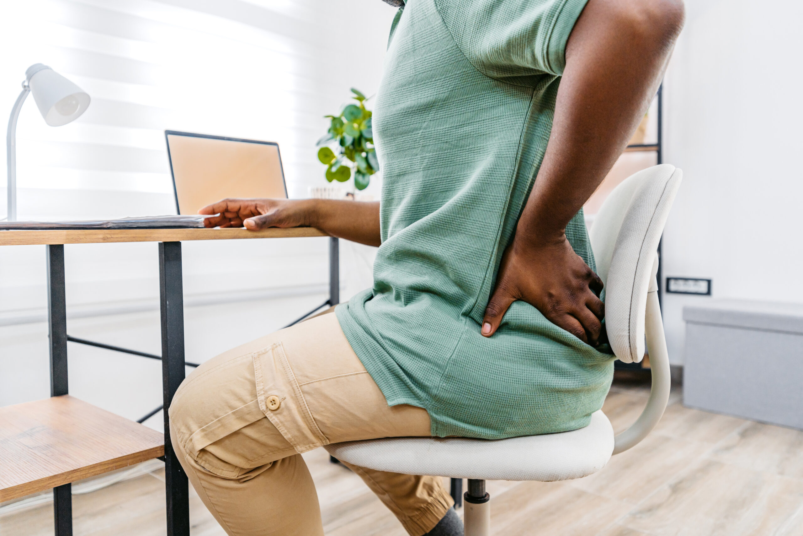 Tired young black man working from home on a laptop and having back pain. Close-up.