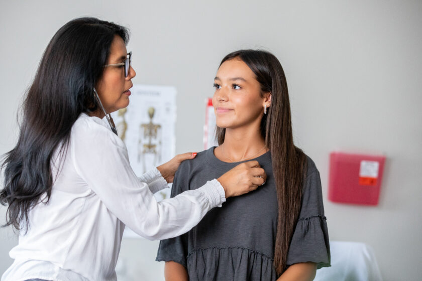 A girl smiles at the woman doctor as she checks her heart.