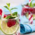 Little glass jars with fresh mint, lemon slice and raspberries refresher concept, over white wooden table with blue napkin