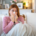Sick young woman blowing her nose on the sofa at home