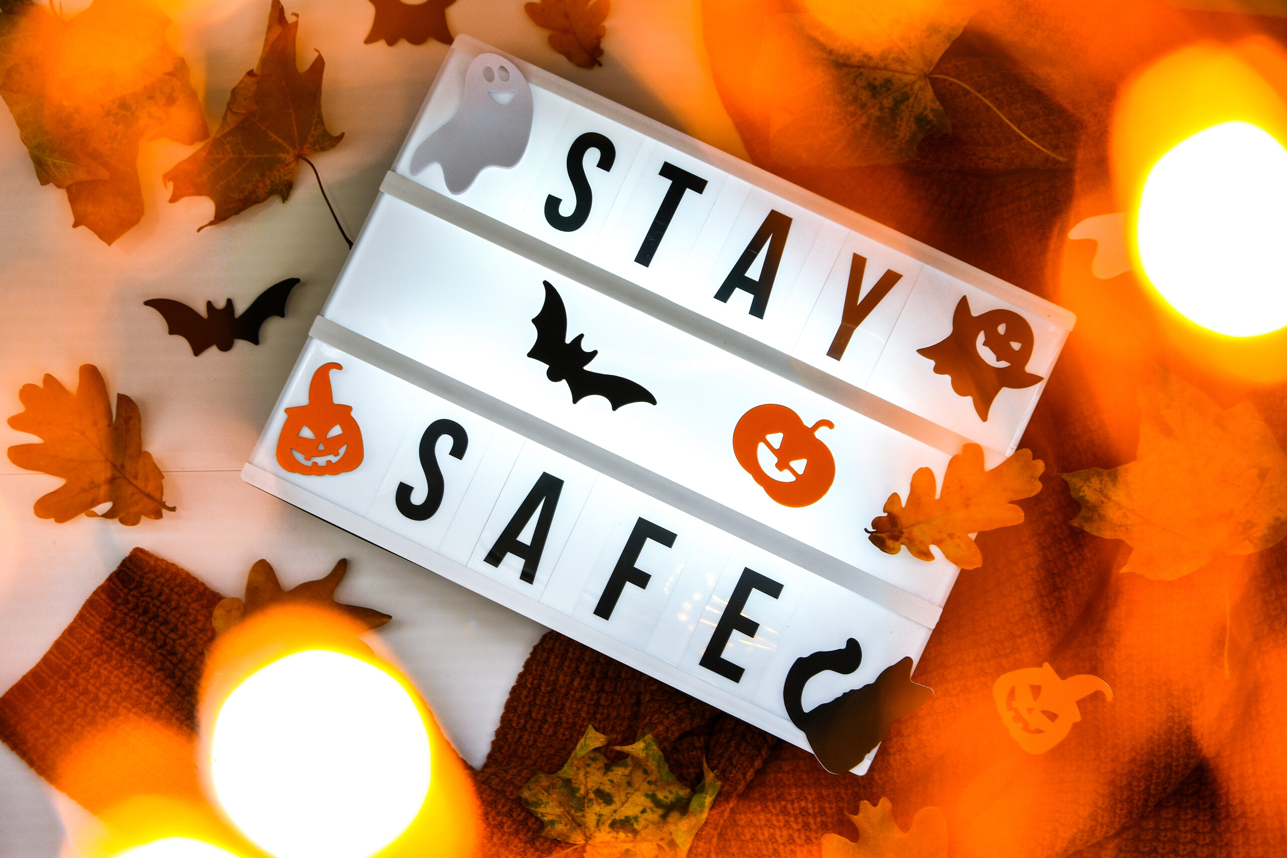Stay safe. Text in white light box, with a background of sweater, dried leaves halloween autumn decoration.